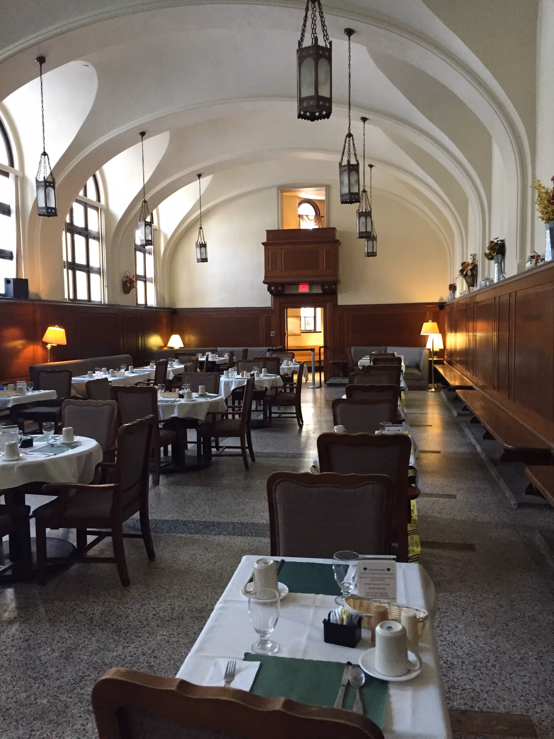 Dining room with multiple set tables, high arched ceiling, hanging lanterns and wood-paneled walls.