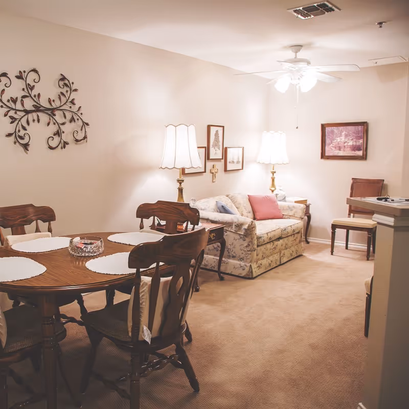 Cozy living and dining area with a wooden dining table, floral sofa, lamps, and wall art.