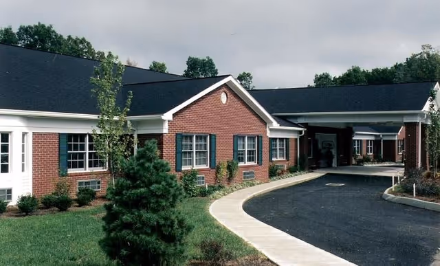 Brick senior living facility with curved driveway and covered entrance under a cloudy sky.