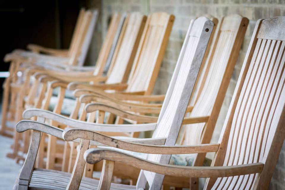 A row of wooden rocking chairs lined up outdoors against a brick wall, with a shallow depth of field focusing on the nearest chairs.