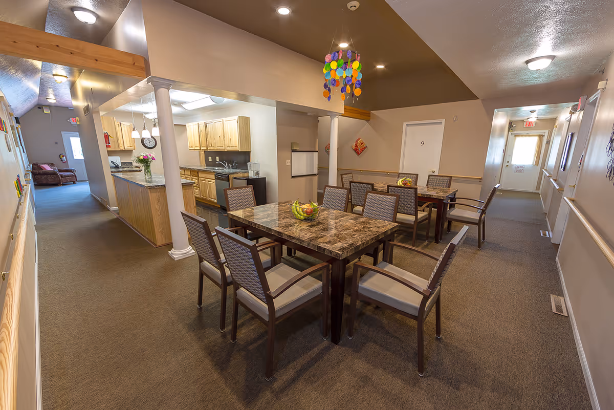 Communal dining room with marble-top tables and chairs next to an open kitchen and hallway.
