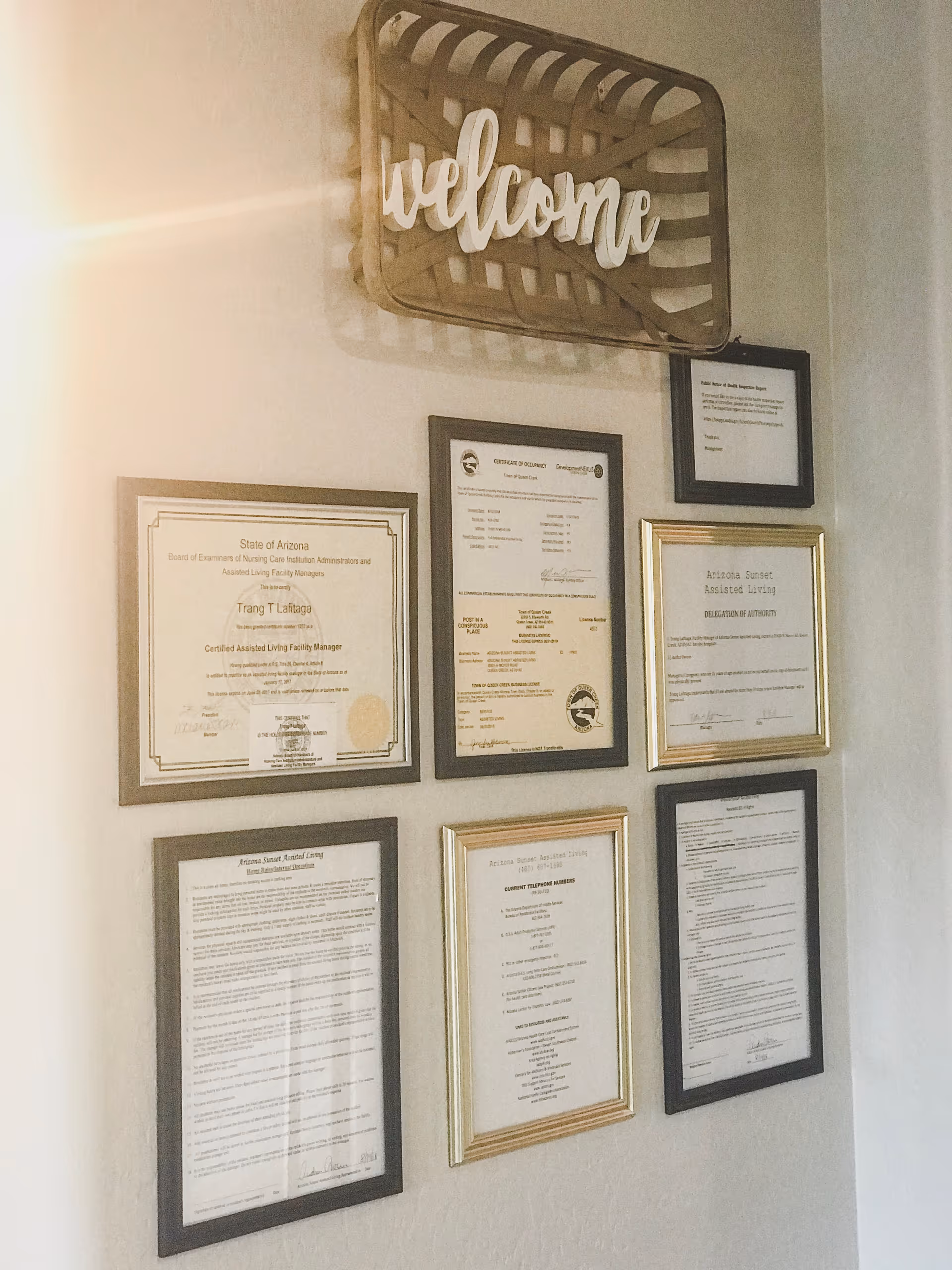 Wall with framed certificates and a decorative "welcome" sign in an assisted living facility.