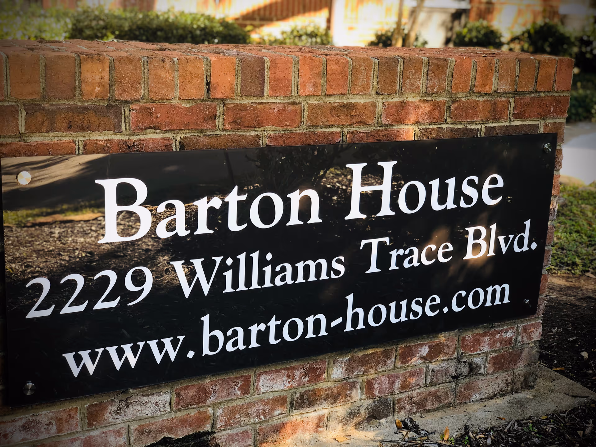 Black sign on brick wall displays Barton House address and website.