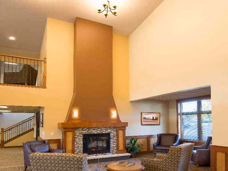 Spacious senior living lounge with a tall central fireplace, seating area and large windows.
