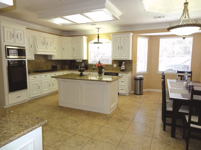 Bright kitchen with white cabinetry, a central island with granite countertops, and an adjacent dining table.
