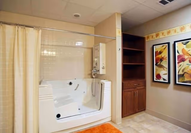 Bathroom with a white walk-in bathtub/shower, beige tiles and curtain, wood shelving cabinet, and framed artwork on the wall.