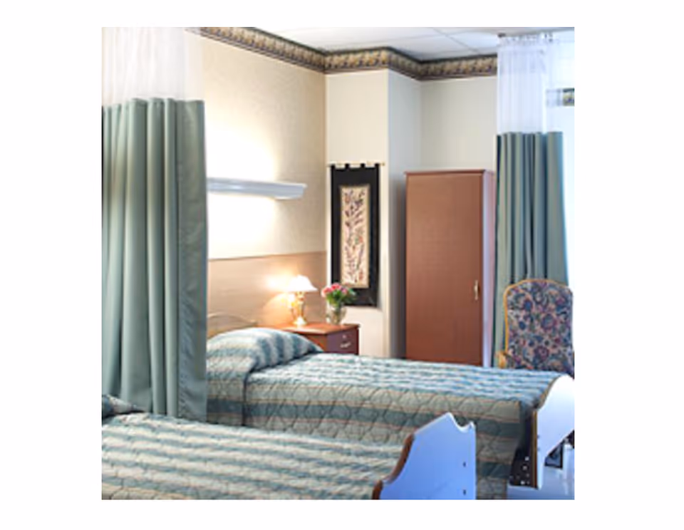 Two hospital-style beds with green linens and privacy curtains in a shared bedroom.
