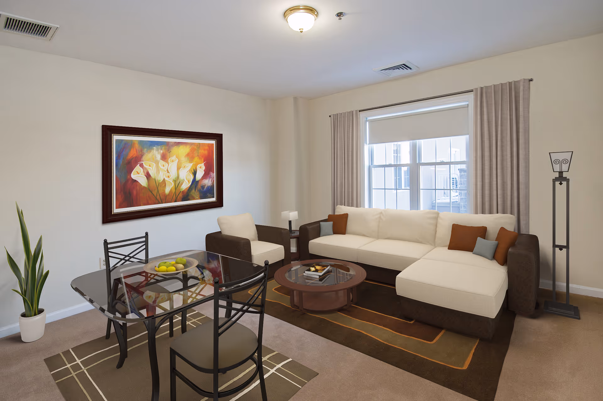 A cozy living room with a large beige and brown sectional sofa adorned with brown and gray pillows, a matching armchair, a round wooden coffee table with books, and a glass dining table with four chairs. The room features a colorful floral painting on the wall, a tall floor lamp, a potted plant, beige curtains, and a window letting in natural light.