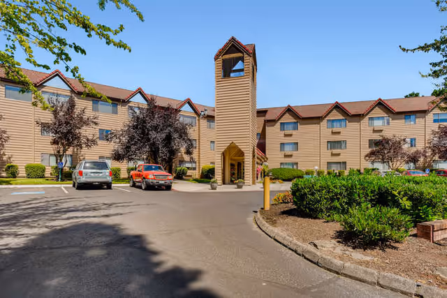 Exterior view of Solista Milwaukie, a beige multi-wing senior living building with tower entrance and driveway.
