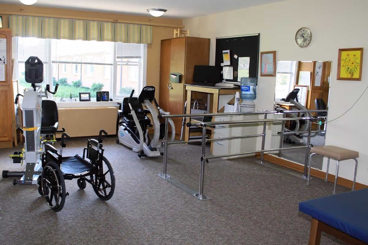 Interior therapy/rehab room with a wheelchair, exercise bikes, parallel bars, and a water cooler.