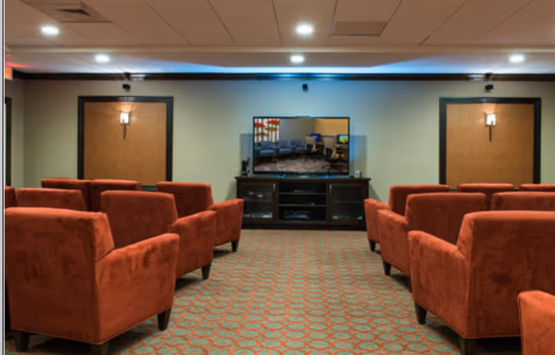 Small media room with rows of red upholstered armchairs facing a television on a cabinet.