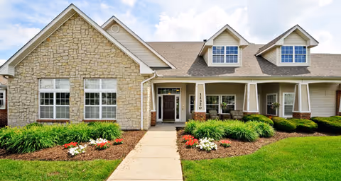 Front exterior of a single-story residential building with stone and siding facade, covered porch, dormer windows, and manicured landscaping.