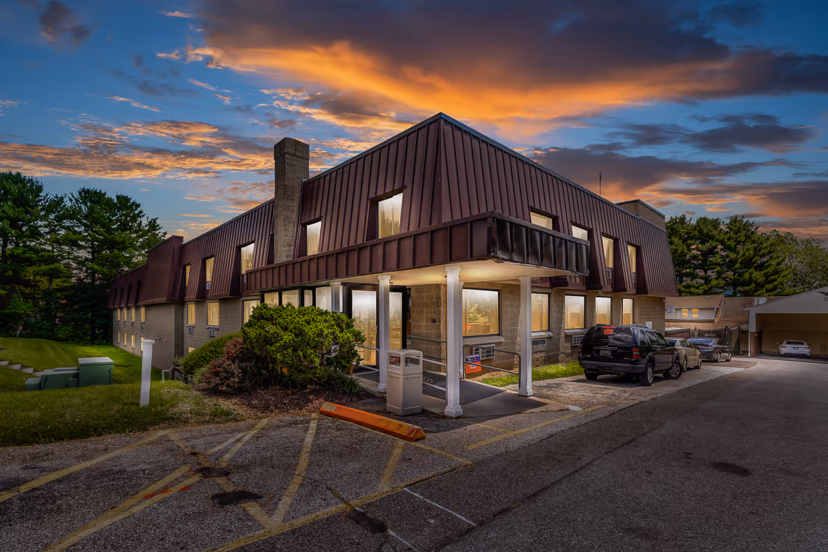Two-story brick senior living facility exterior at dusk with a covered entrance, parked cars, and landscaped grounds.