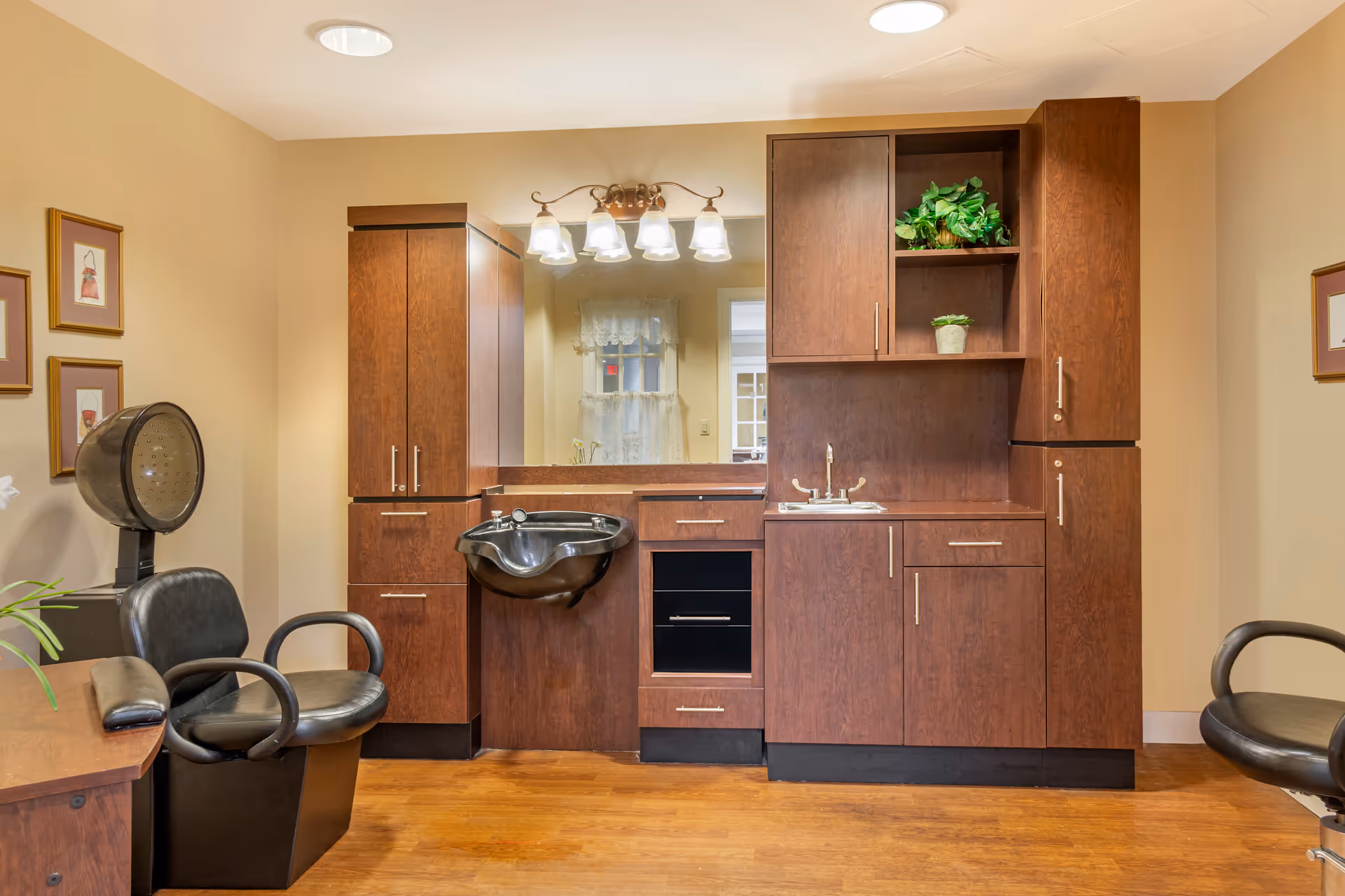 A hair salon station with wooden cabinets, a black shampoo sink, styling chairs, and overhead lights.
