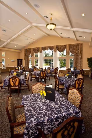 Spacious dining room with patterned tables, chairs, and large windows with draped curtains.