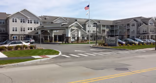 Exterior view of The Highlands Gracious Retirement Living with entrance, parking, and flagpole.