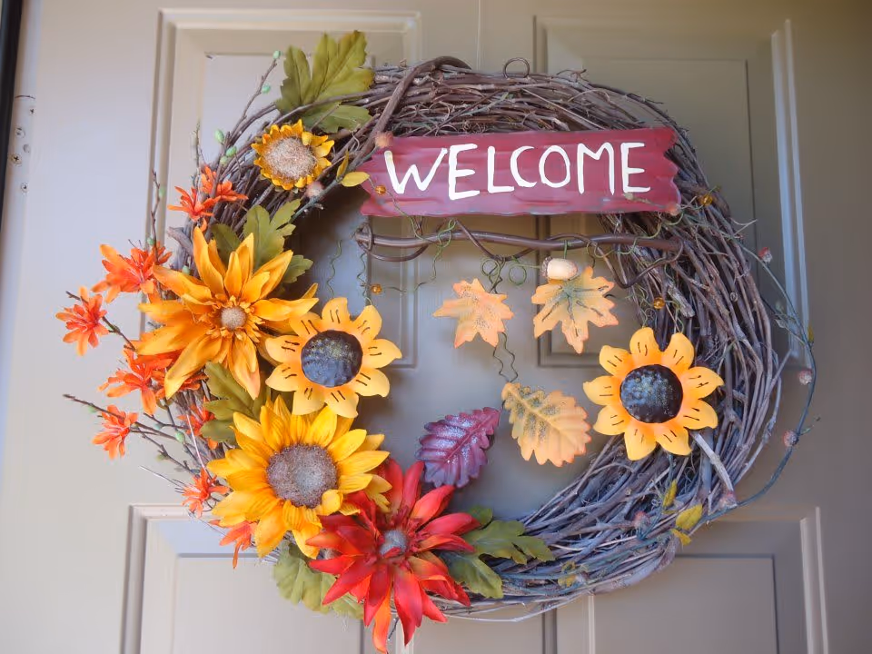 A decorative autumn wreath with sunflowers and a 'WELCOME' sign hanging on a beige door.