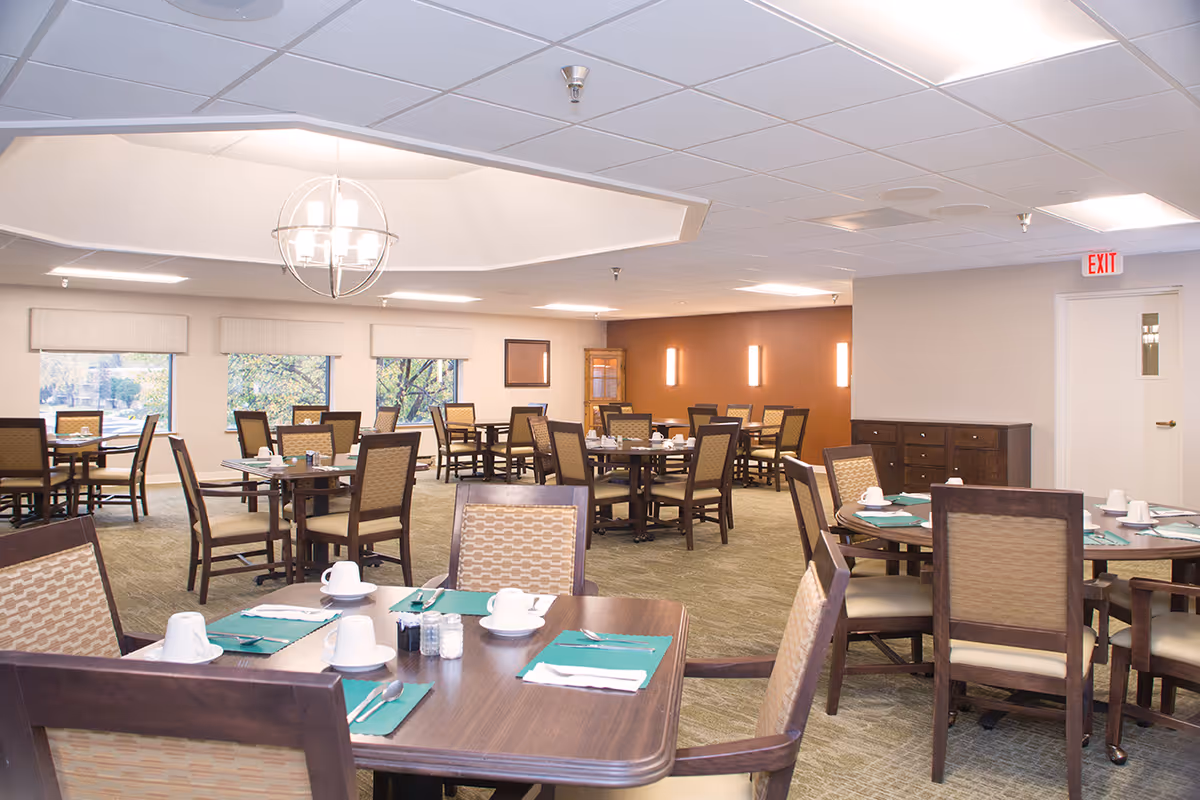Bright, spacious dining room with multiple tables set for meals and upholstered chairs.
