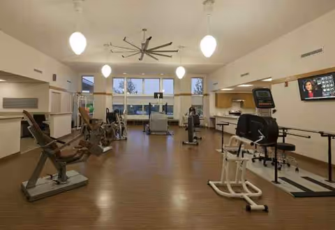 A spacious senior fitness center with cardio machines and warm wooden flooring.