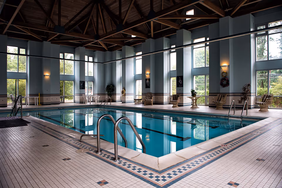 Indoor pool area in a senior living facility with blue water, tiled deck, and windows.