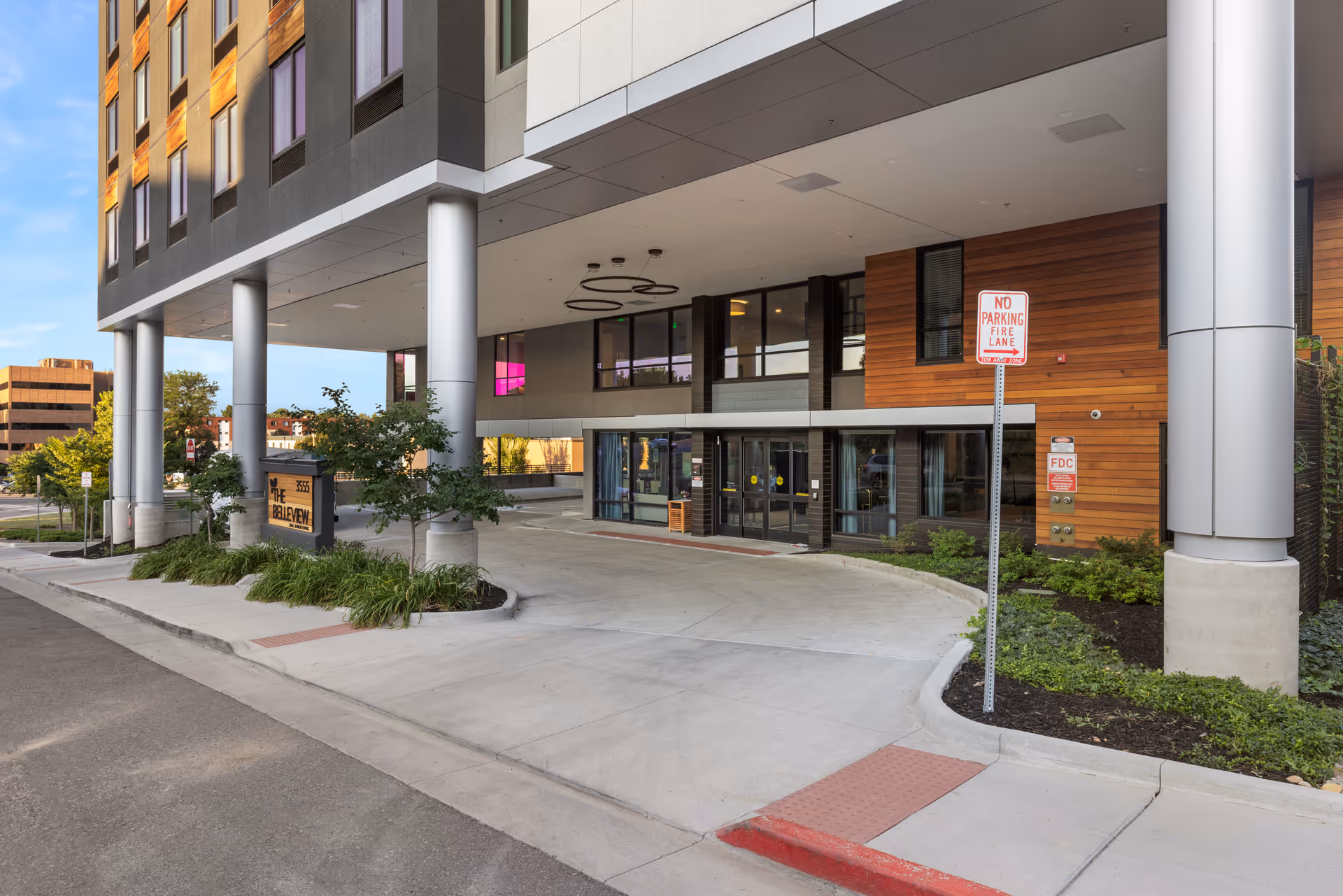 Covered entrance and porte-cochere of The Belleview senior living building with large pillars, landscaping and a 'No Parking Fire Lane' sign.