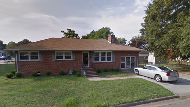 Single-story brick building with driveway, parked car, and a grassy lawn.
