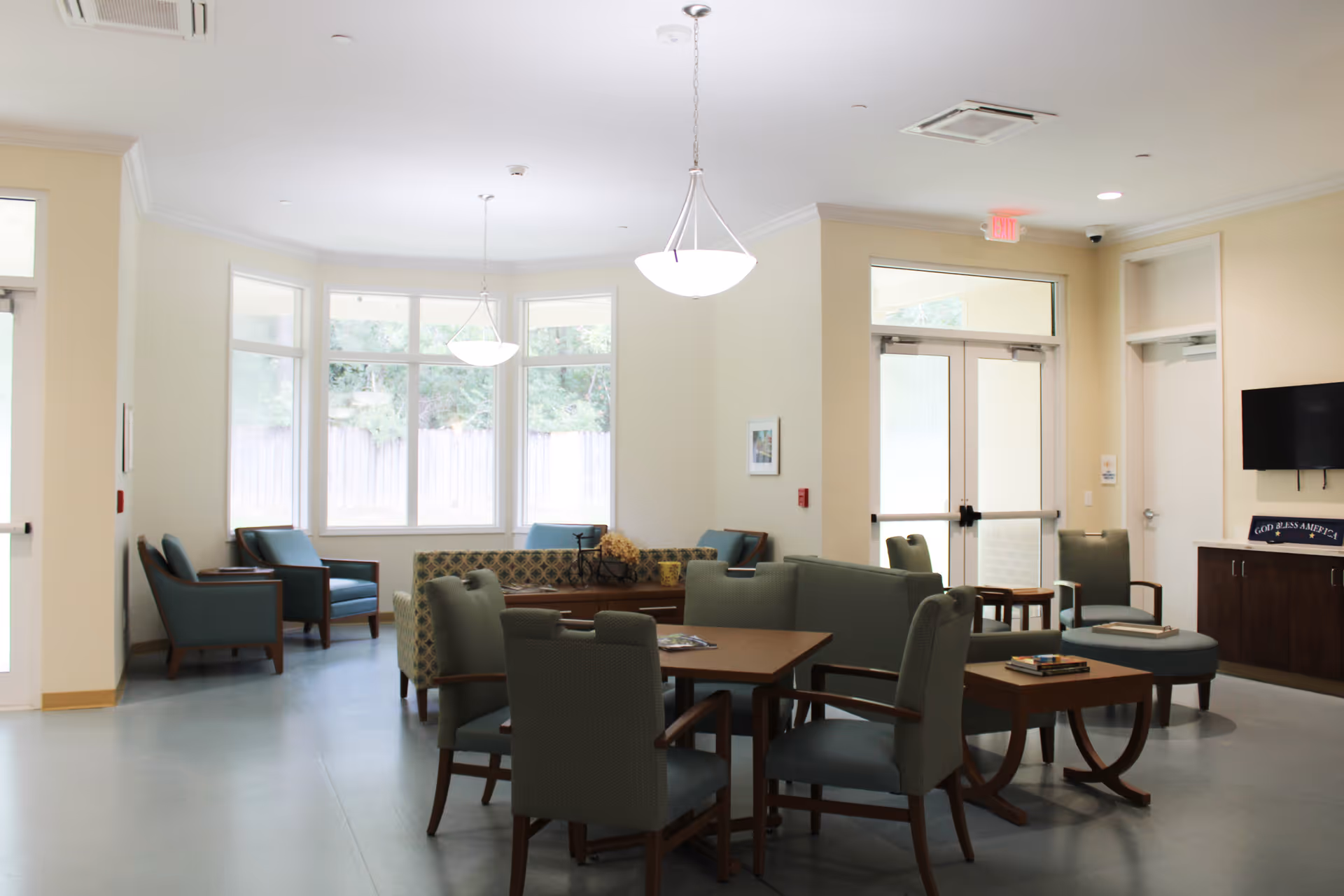 Bright common room with tables, armchairs, sofas and large windows in an assisted living facility.
