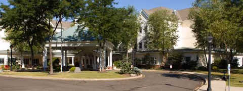 Exterior view of Complete Care at Whispering Woods' front entrance with trees and porte-cochère.