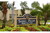 Entrance sign for Sabal Palms Health Care Center surrounded by palm trees and greenery, with a beige building in the background.