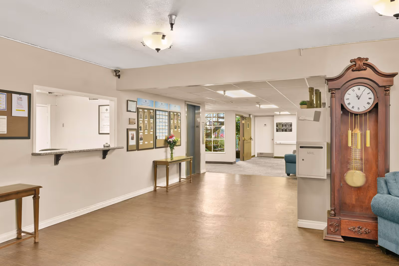 Interior reception lobby of a retirement community with a check-in window, bulletin boards, small tables, seating and a grandfather clock.