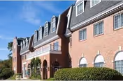 Brick senior living facility with arched windows and manicured hedges under a blue sky.