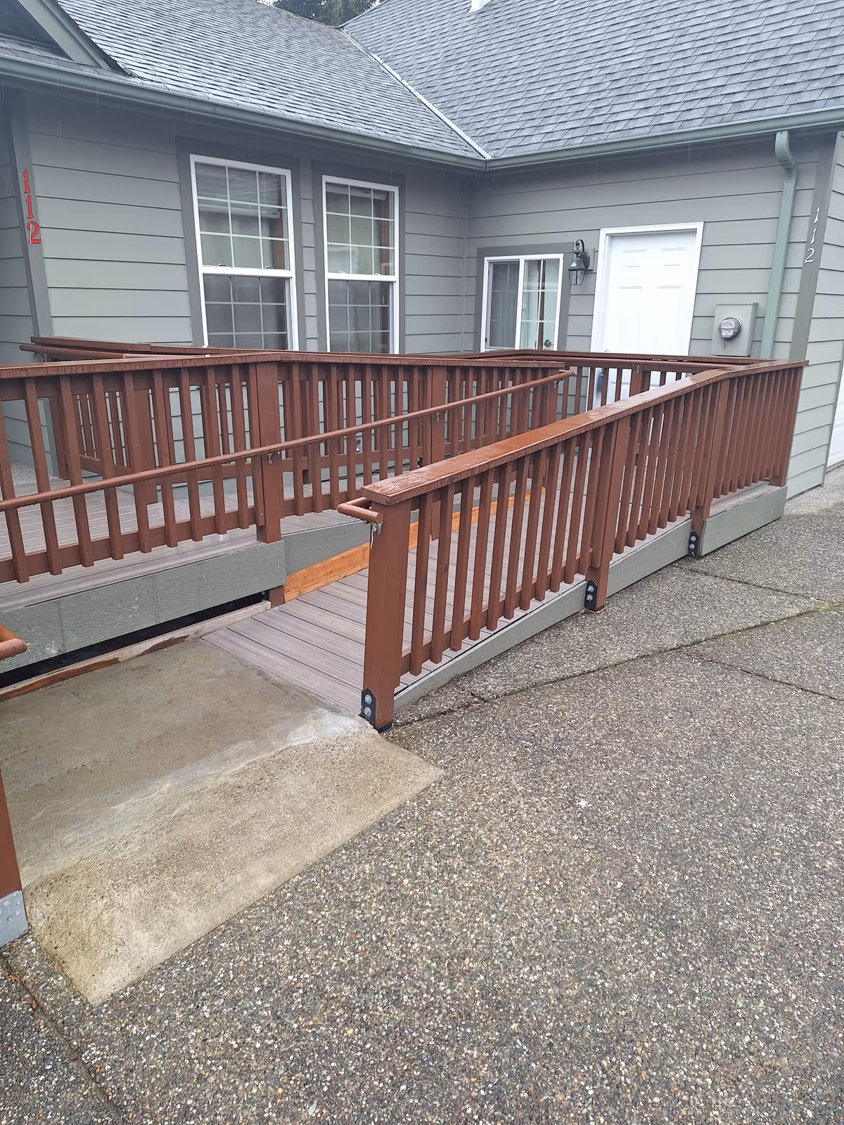 Wooden accessibility ramp leading to the entrance of a gray single-story building with windows and a white door.