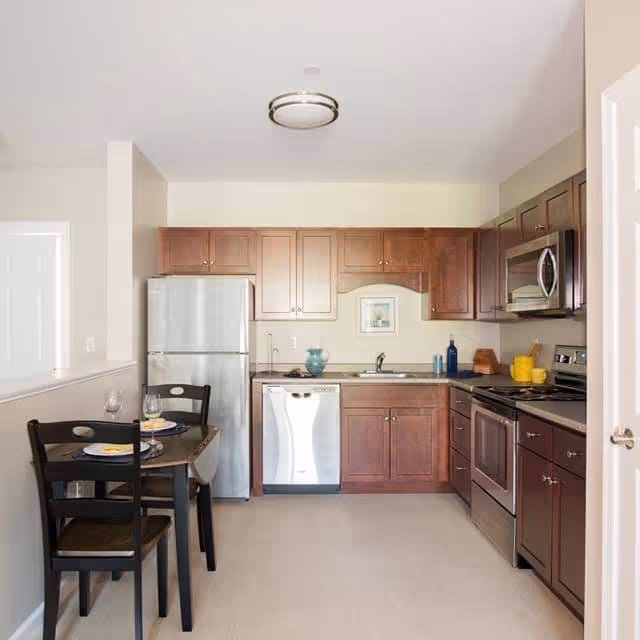 Small modern kitchen with dark wood cabinets, stainless steel appliances, and a small dining table set for two.