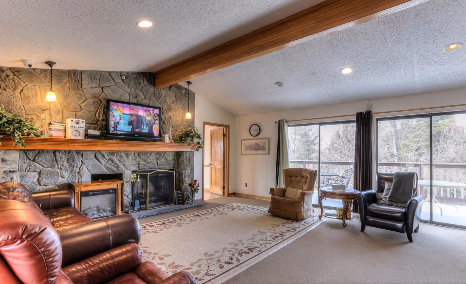 Cozy living room with stone fireplace, TV, leather seating, and sliding glass door to deck.
