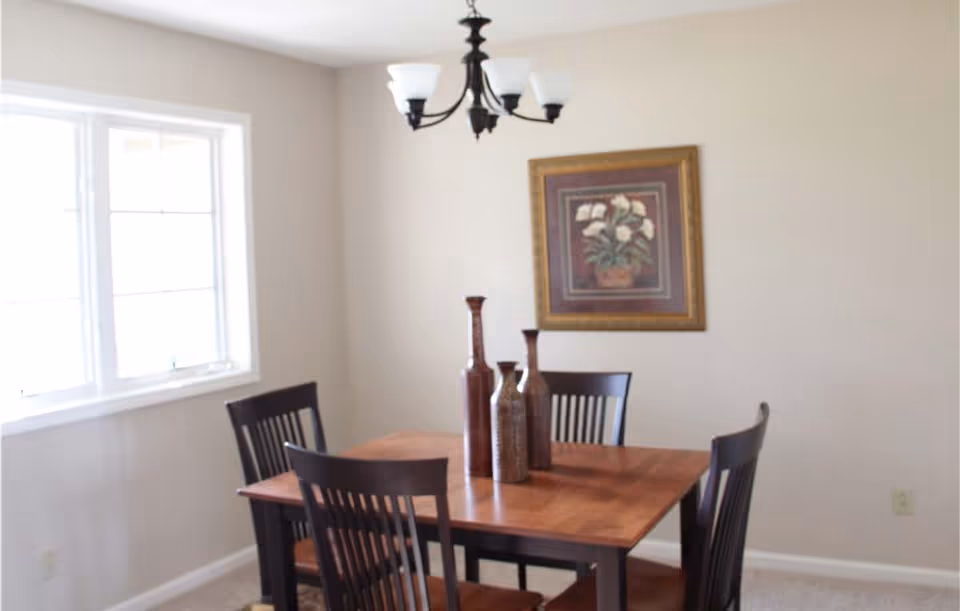 Dining room with a wooden table and chairs, decorative vases, a chandelier, and a framed floral painting on the wall.