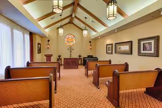 Interior chapel-like room with wooden pews, high vaulted ceiling, and hanging lanterns.