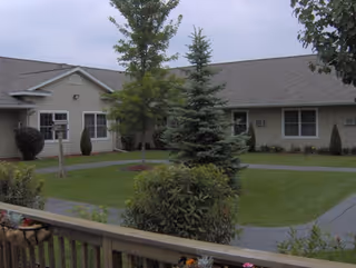 Exterior view of a Spring Arbor Assisted Living building with lawn, trees, and a wooden deck.