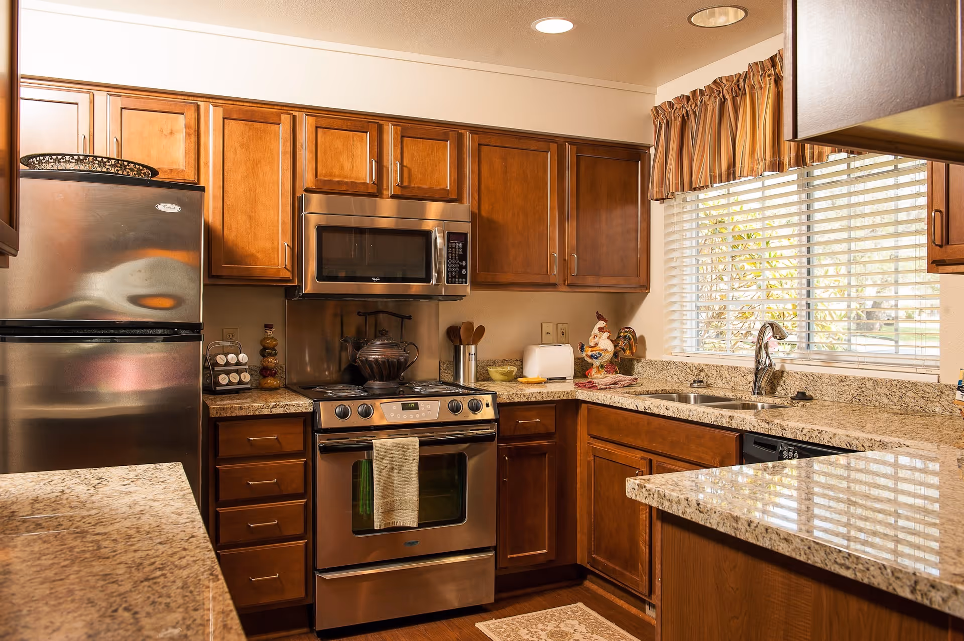 Well-lit kitchen with stainless steel appliances, wooden cabinets, granite countertops, and a window above the sink.