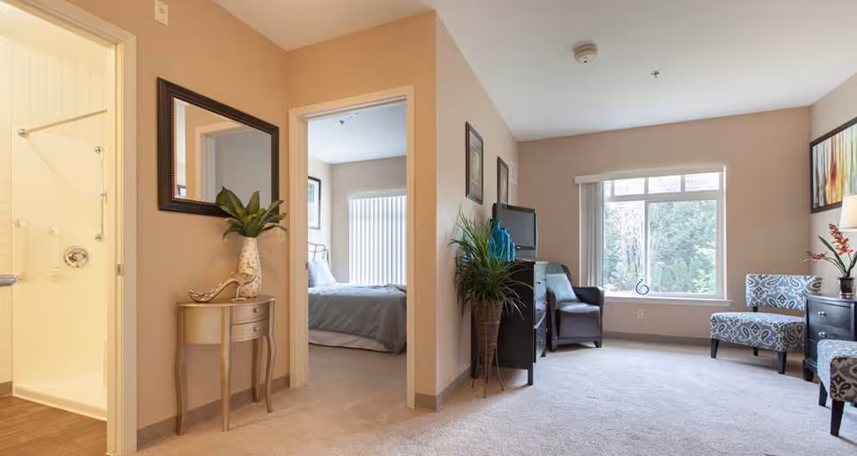 Bright living room with seating, a TV, plants, and doorways leading to a bedroom and bathroom.