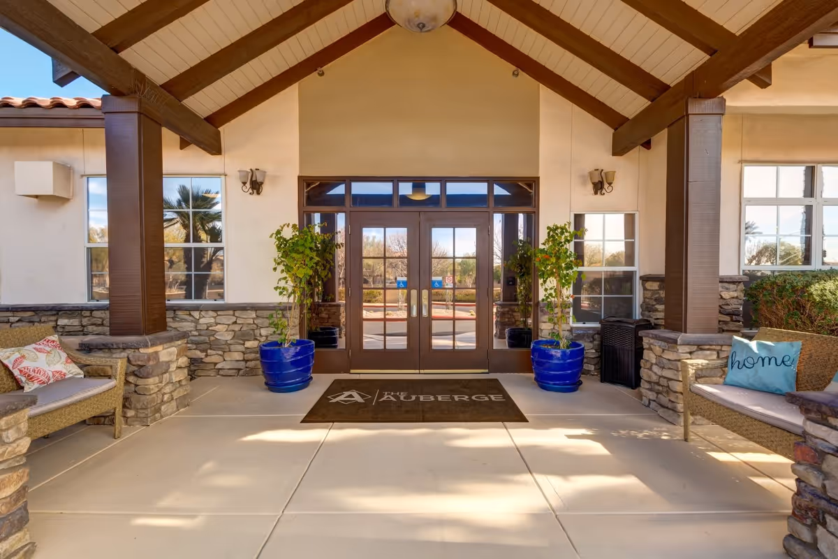 Covered main entrance with double glass doors, potted plants, seating benches and an Auberge doormat.