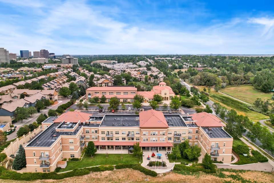 Aerial exterior view of The Inn at Greenwood Village senior living building with terracotta roofs, surrounding homes, and green space.