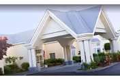 Entrance area of Richmond Beach Rehab facility showing a covered driveway with white pillars and a peaked roof, surrounded by landscaped greenery and a clear sky.