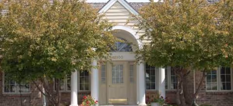 Front view of a brick senior living building with arches, columns, and trees.
