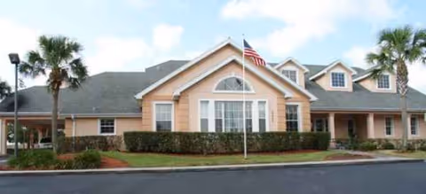 Senior living facility building exterior with a flag, palm trees, and manicured lawn.