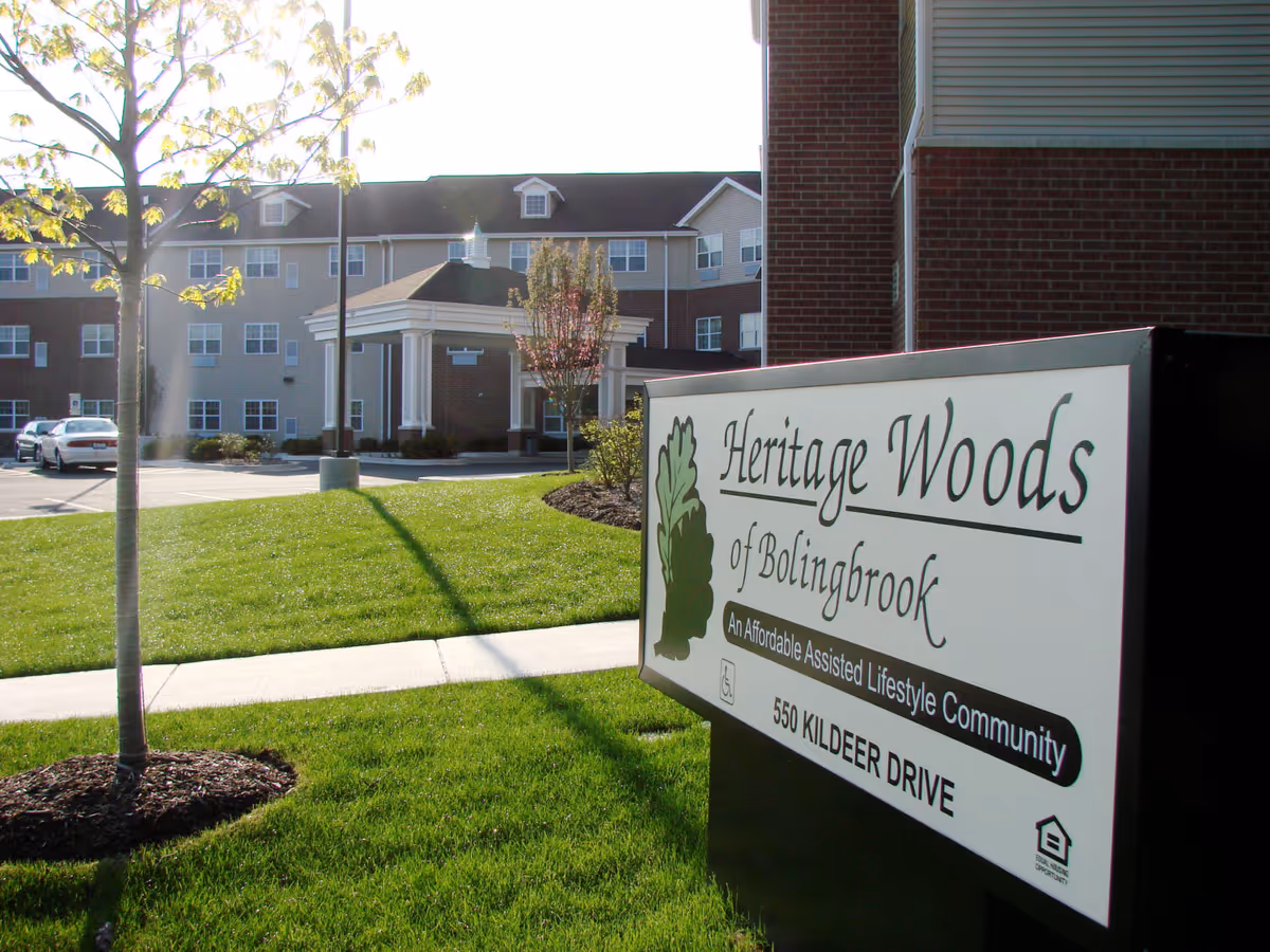 Exterior view of the Heritage Woods of Bolingbrook building with its entrance driveway and a large facility sign in the foreground.