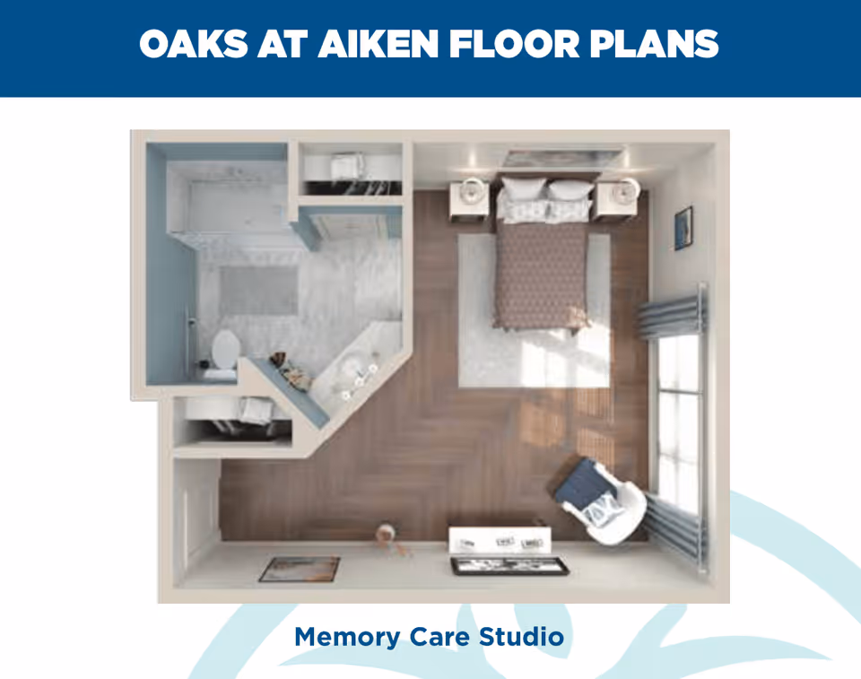 Top-down view of a memory care studio floor plan at Oaks at Aiken, showing a bedroom area with a bed, two nightstands, a chair near a window with curtains, and an adjacent bathroom with a shower, toilet, and sink.
