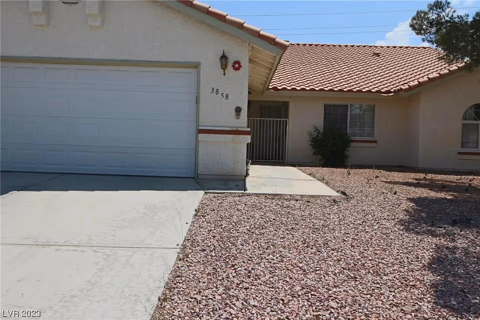 Front exterior of a single-story house with a garage door, tiled roof, gated entry, and rock landscaping.