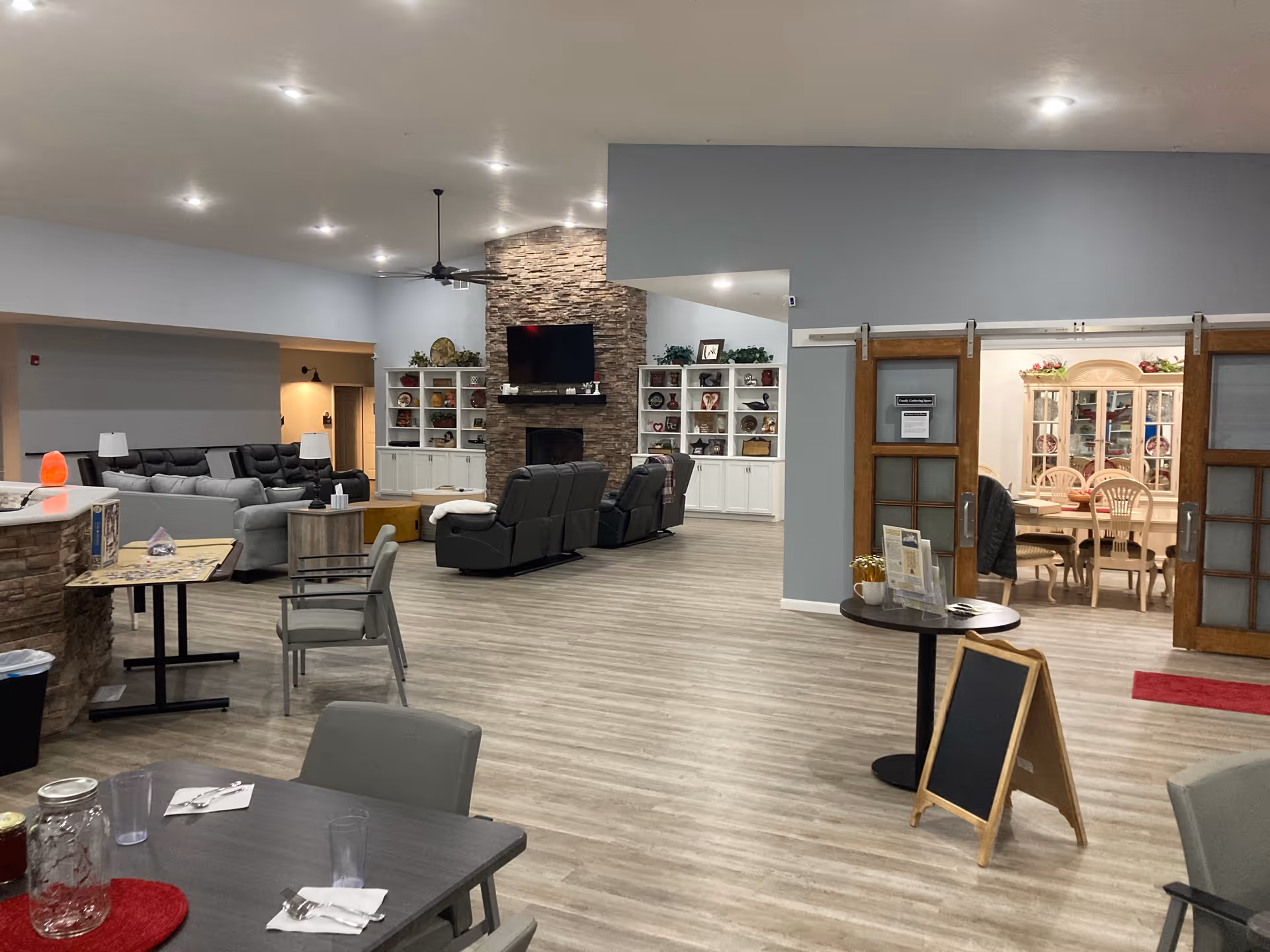 Spacious senior living lounge with couches, stone fireplace, and dining area beyond.