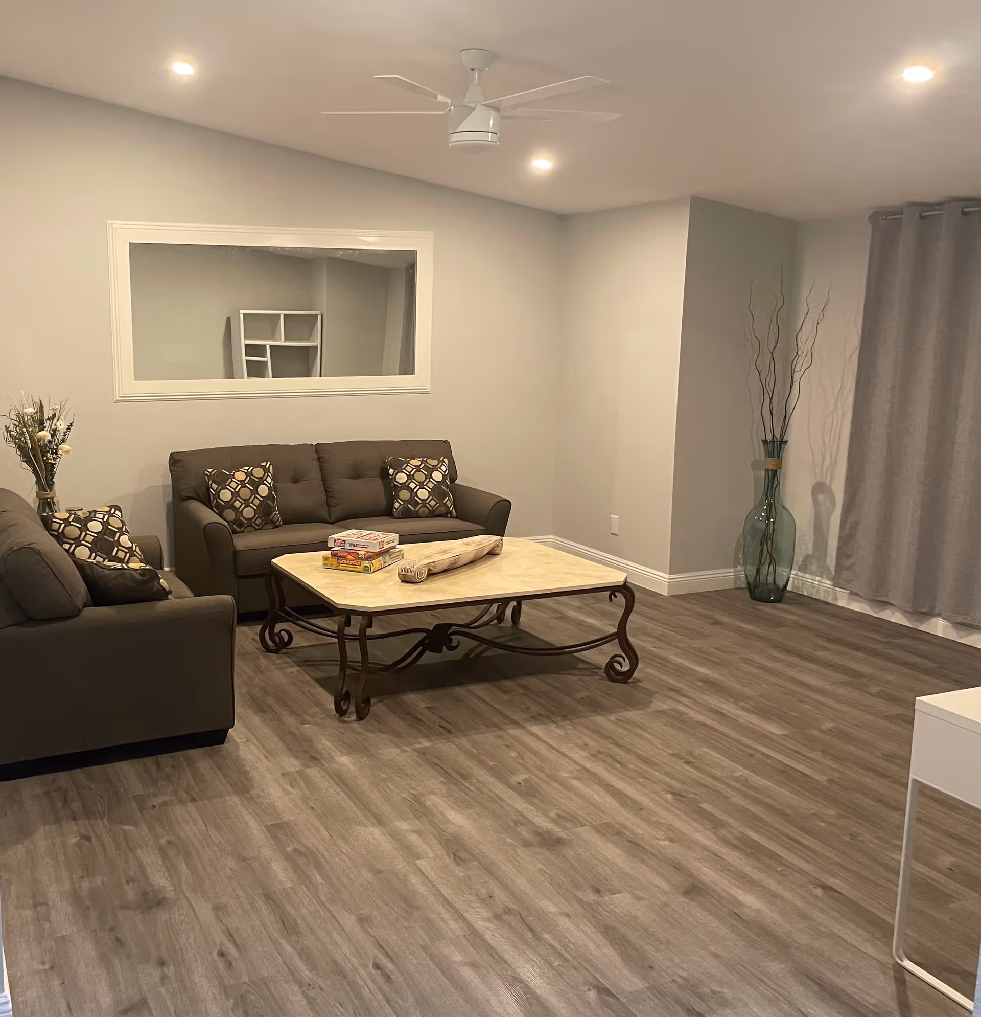 Well-lit living room with two gray sofas, a central coffee table, patterned throw pillows and a large decorative floor vase.