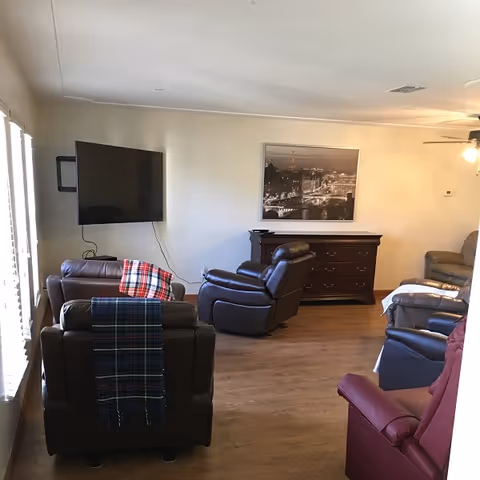 Cozy living room with several recliner chairs arranged facing a wall-mounted TV and a dresser topped by a framed cityscape photo.